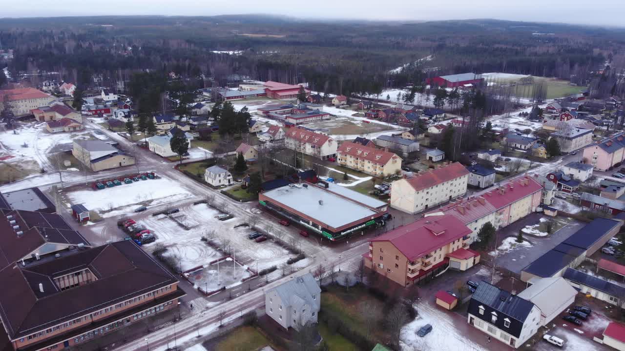 Drone slowly moving forward over the calm town of Vansbro, Sweden. A singel car moving in the streets. Overcast with some snow still on the ground. Aerial shot