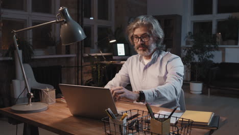man working late at night, closing laptop and adjusting desk lamp