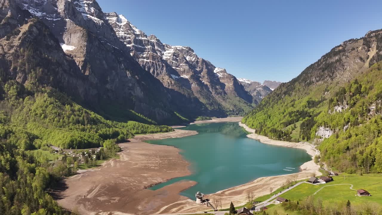 The turquoise Klöntalersee is framed by towering, snow-dusted peaks in the Klöntal, Schweiz, revealing wide, exposed banks. Concept of glacial basin solitude and majesty