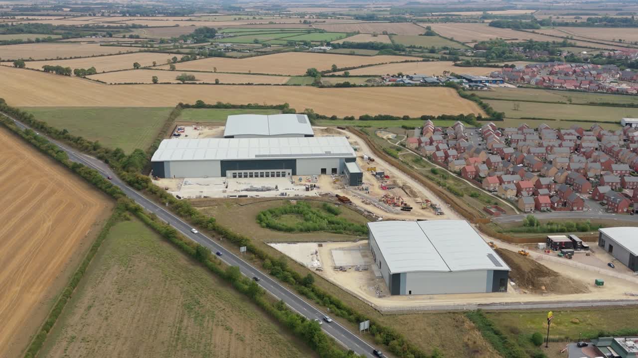 High altitude drone footage showing industrial plants with trucks and trailers for goods transport operating beside main road network in England UK