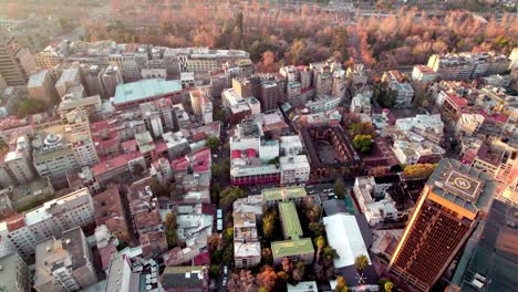 aerial dolly in of lastarria neighborhood buildings and forestal park autumnal trees in background at golden hour, santiago, chile