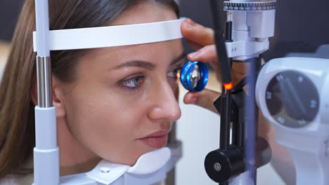 female patient holds her head on a device for eyesight check. the bright ray of light comes to the woman's eye. close up.