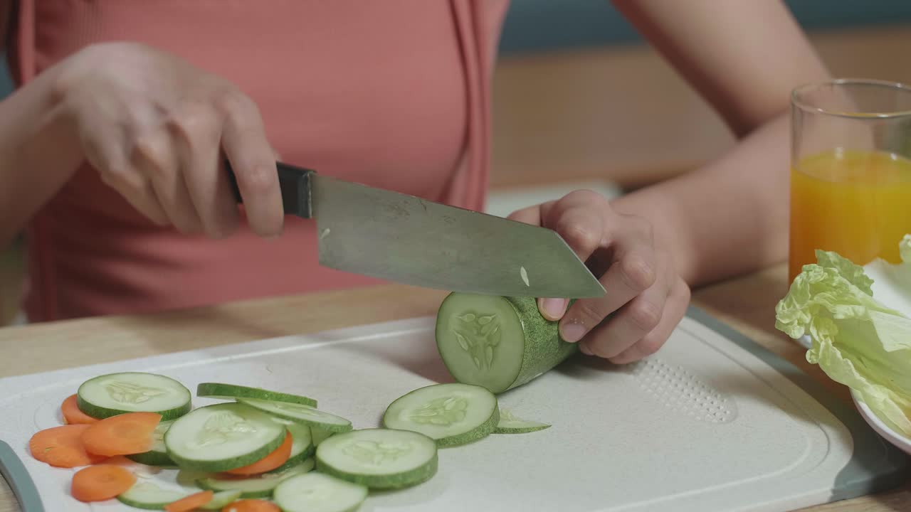Close Up Of Woman'S Hands Holding A Knife And Slicing Cucumber On The Chopping Board In The Kitchen