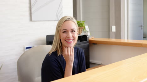 smiling woman sitting at reception desk in medical clinic, looking at camera