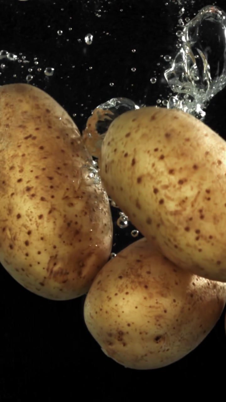 Patate fresche che cadono nell'acqua con bolle su sfondo nero.