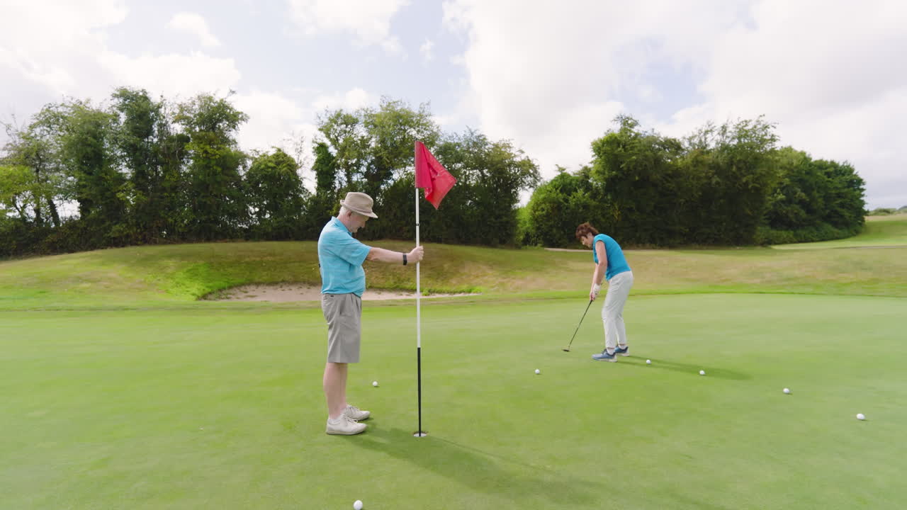 Male and female golf players playing golf and knocking golf ball into cup on golf course