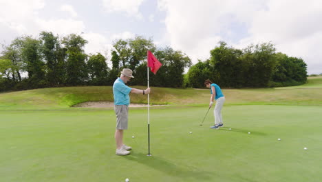 male and female golf players playing golf and knocking golf ball into cup on golf course