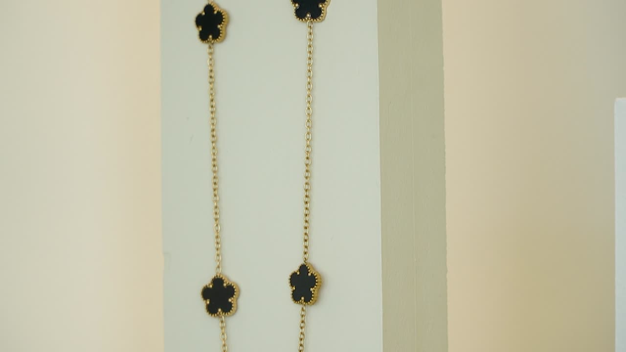 A stunning gold necklace featuring a black pendant is displayed against a soft, neutral background. The elegant design shines in natural light, highlighting its beauty