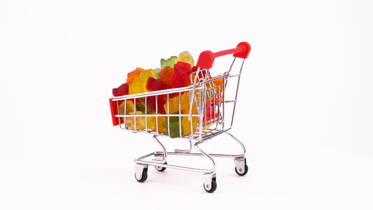 Supermarket trolley with bear shaped sweet gummy candies pile rotating on the turntable. Isolated on the white background. Close-up. Macro.
