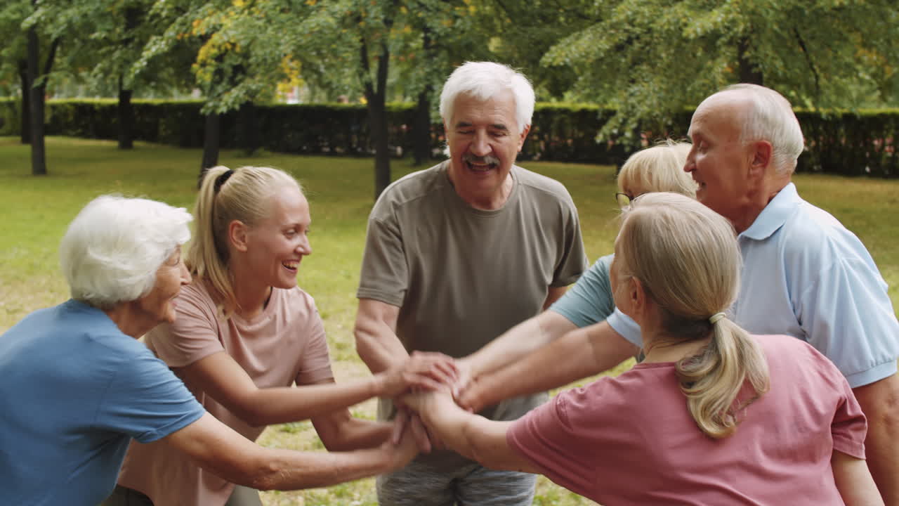 즐거운 노인들이 공원에서 여성 트레이너와 손을 고 있습니다.