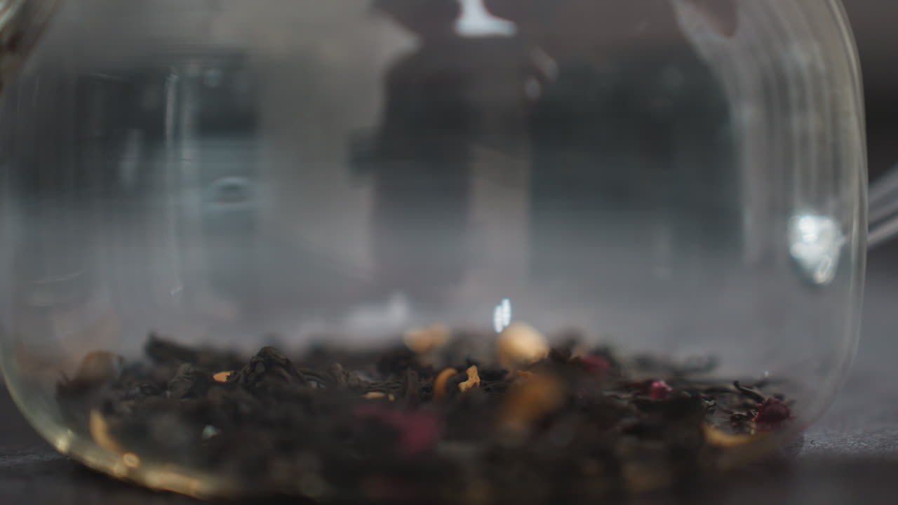 Glass Teapot With Loose Tea Leaves Settling On Base, Warm Kitchen Light, Shallow Depth, Slow Infusion, Steam Haze, Reflective Surface, Close Macro On Leaf Texture And Amber Tint, Cozy Meditative Mood