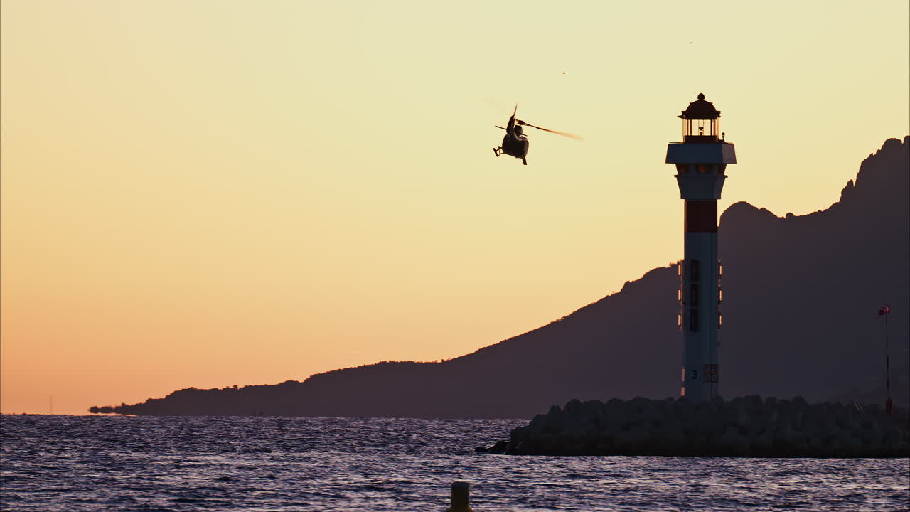 View of a helicopter taking of at sunset near a lighthouse with the mountains on the background in the south of France