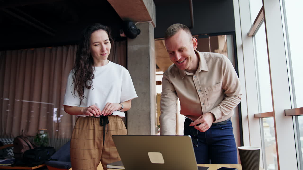 Male and female colleagues collaborating in the office. Workmates look at laptop discussing it. Low angle view.