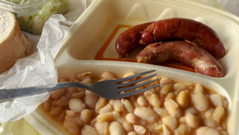 comida para llevar en envases de espuma de poliestireno: frijoles blancos y salchichas con ensalada de repollo rallado, pie de mano de vista superior