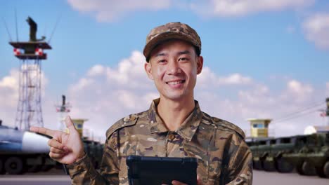 close up of asian man soldier using a tablet and pointing to side while standing at military camp