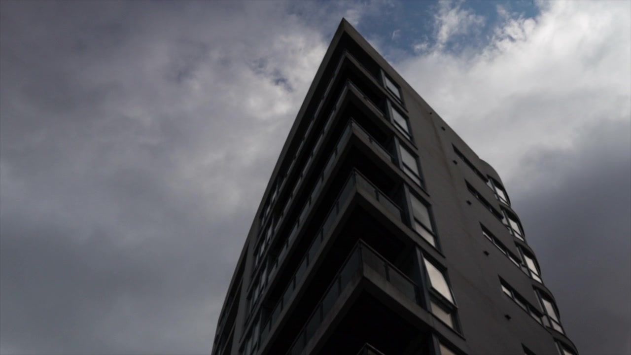 Cielo azul nublado inclinándose hacia abajo para revelar un edificio de apartamentos moderno en un ángulo.