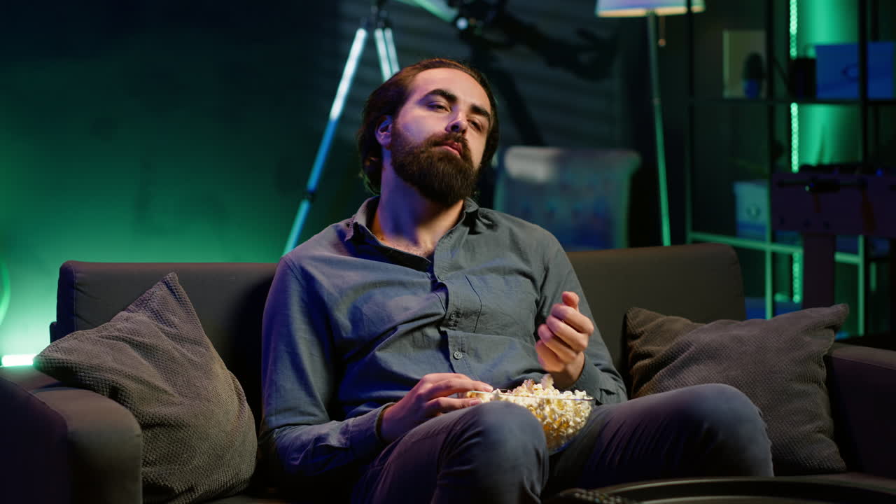 hombre fatigado viendo programas en la televisión tarde en la noche y comiendo palomitas de maíz