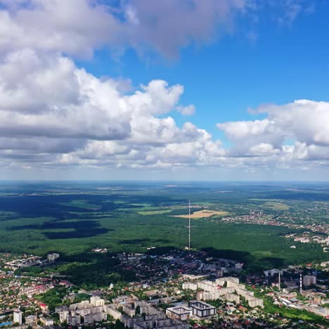 panoramic view of a city among green nature. cityscape under blue sky with white clouds. beautiful scenery of a town near fields. aerial view.