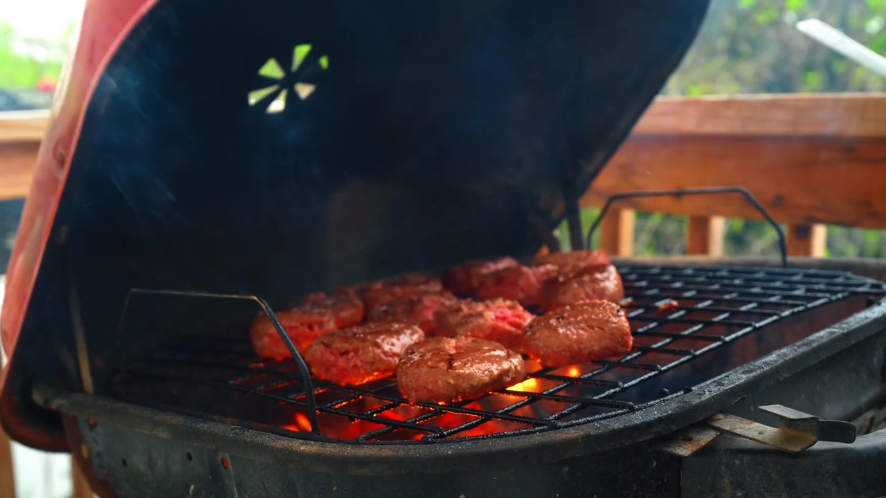 Coperchio metallico rosso chiuso di un barbecue da esterno. Vista laterale di un coperchio rosso di un grill portatile con manico nero su una terrazza di legno.