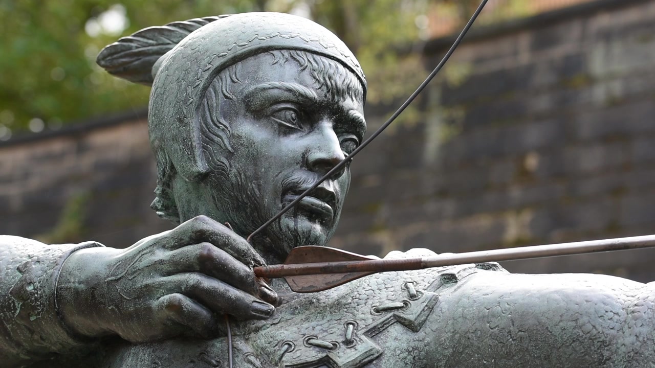 Robin Hood heykeli, Nottingham, İngiltere'deki Castle Yolu üzerinde gururla duruyor ve okunu Nottingham Kalesi'nin tarihi kale kapısına doğru hedefliyor.