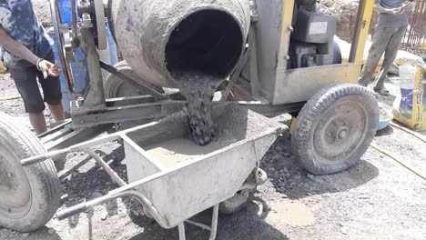 a close-up view of an diesel concrete mixer pouring wet cement into the wheelbarrow at the construction site in india