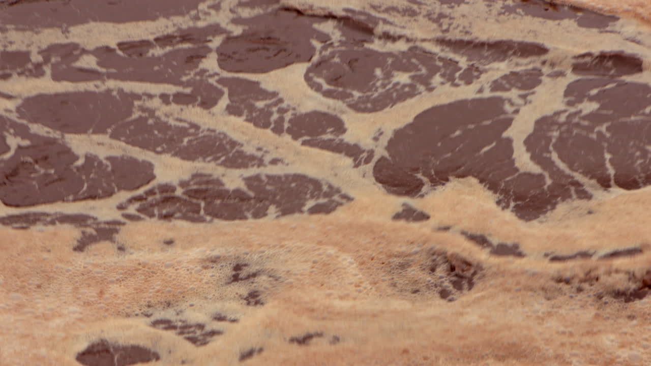 Water churns and froths vigorously in an aeration basin at a wastewater treatment plant, moving through the treatment process in a dynamic, industrial flow