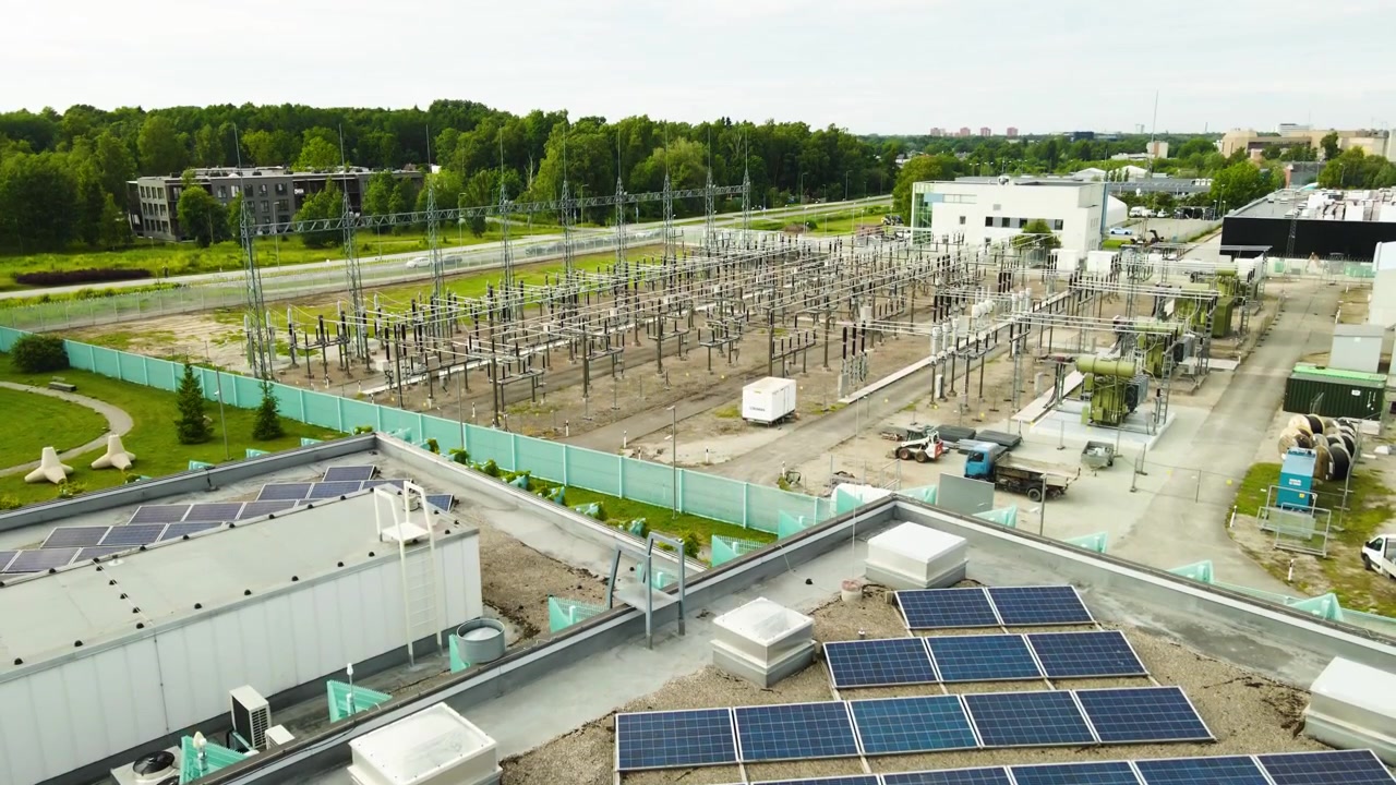 Imagens aéreas de uma subestação elétrica de alta voltagem com transformadores e painéis solares no telhado de um edifício. Apresentando a geração de energia renovável e a infraestrutura de distribuição de eletricidade.