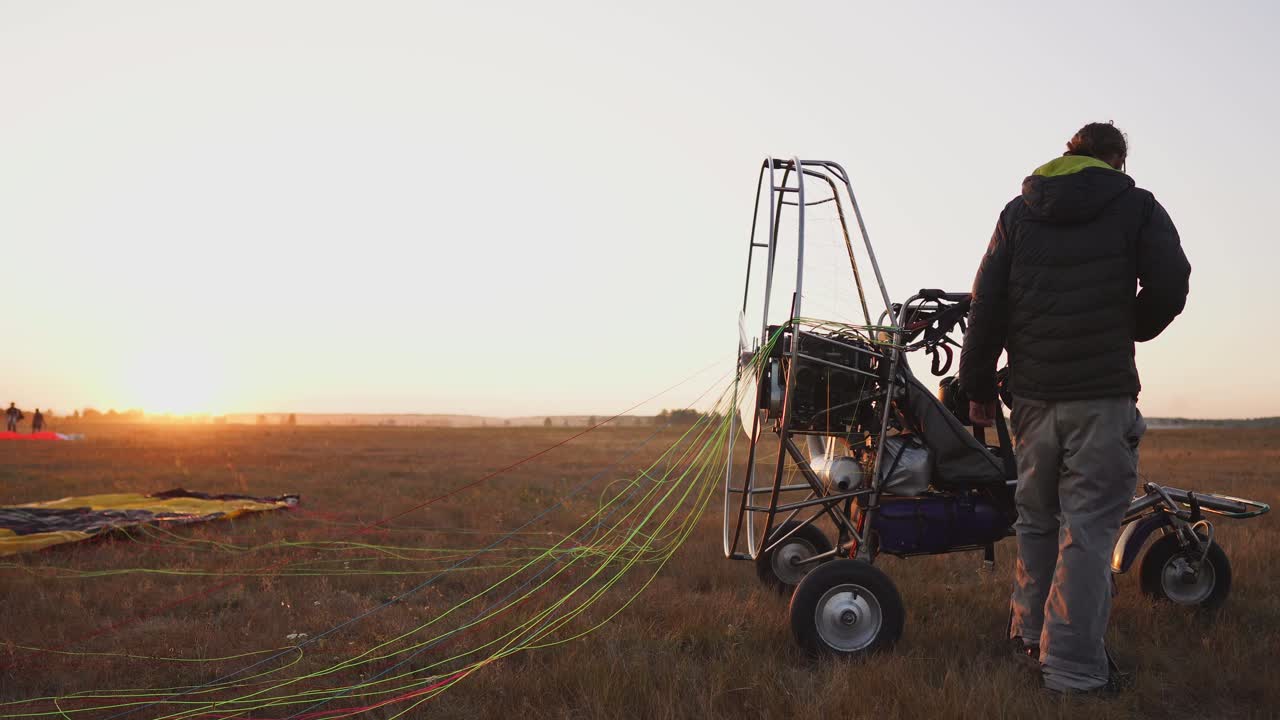모터 패러글라이더의 남자 조종사가 패러글라이더의 몸에 낙하산을 부착하여 비행을 준비하고 장비를 확인합니다.