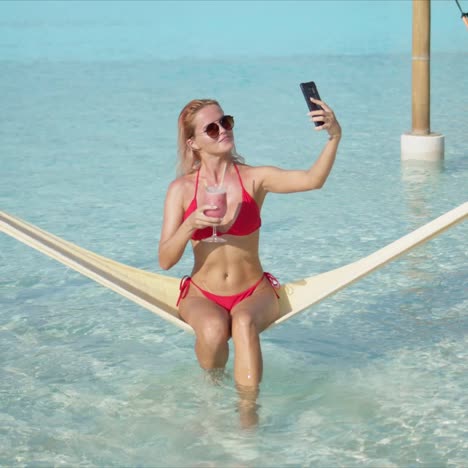 Cheerful-woman-with-cocktail-taking-selfie-on-hammock