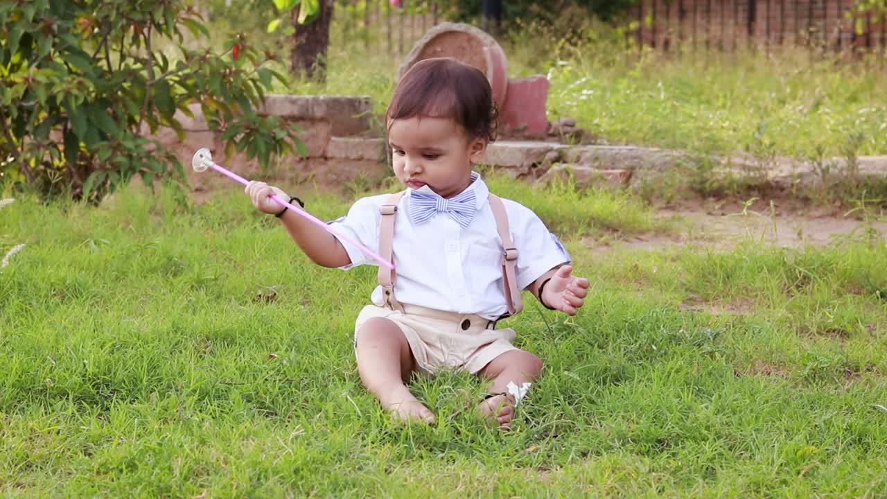 Balita laki-laki lucu terisolasi dengan pakaian putih bermain di taman dari sudut datar.