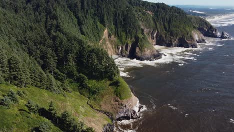 Counterclockwise-drone-shot-of-waves-crashing-against-rocky,-tree-covered-cliffs-on-the-Oregon-coast