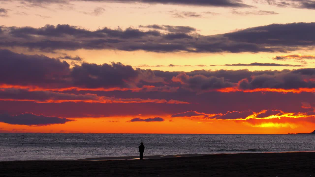 espectacular amanecer en la playa con un hombre mayor recortado contra el mar plateado al amanecer