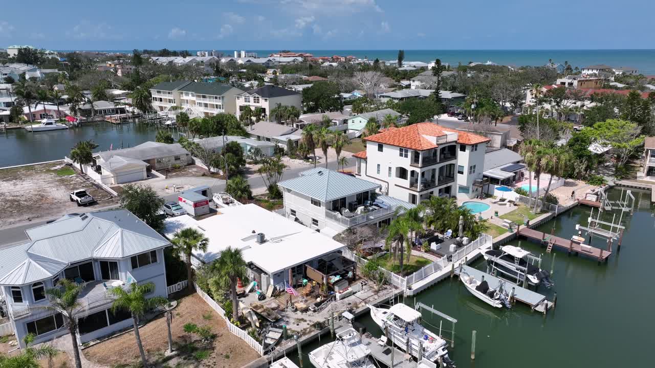 Luxury houses and villas with waving american flag and private yachts at river pier in Indian Rocks beach, Florida. Palm trees in noble neighborhood. Descend drone wide shot. Patriotic rich family.