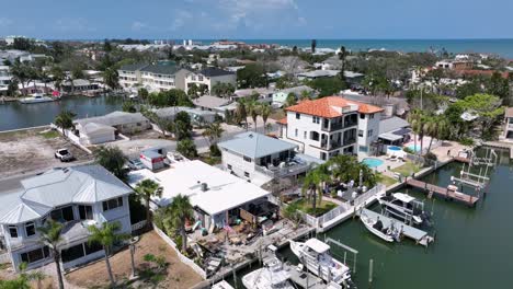 luxury houses and villas with waving american flag and private yachts at river pier in indian rocks beach, florida. palm trees in noble neighborhood. descend drone wide shot. patriotic rich family.