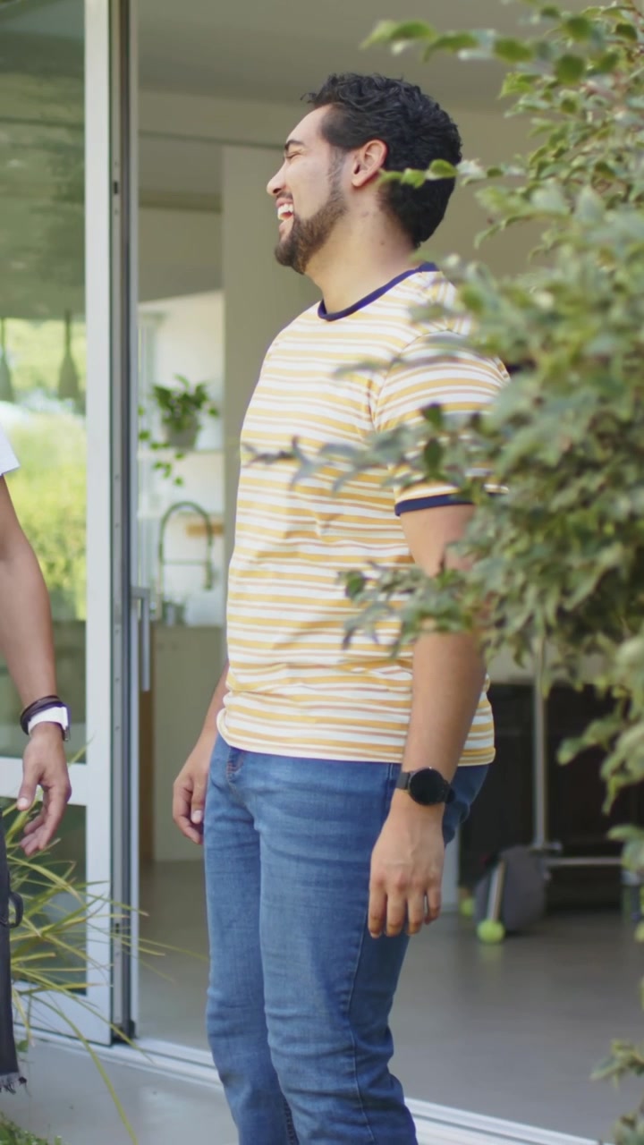 Video vertical: Puerta corrediza abriéndose, hombre con camiseta de rayas saliendo al patio de casa, conversando.