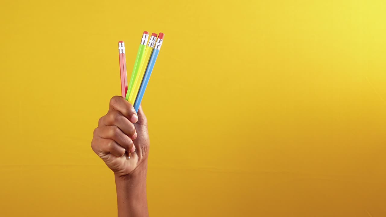 mano con lápices de colores en el fondo amarillo