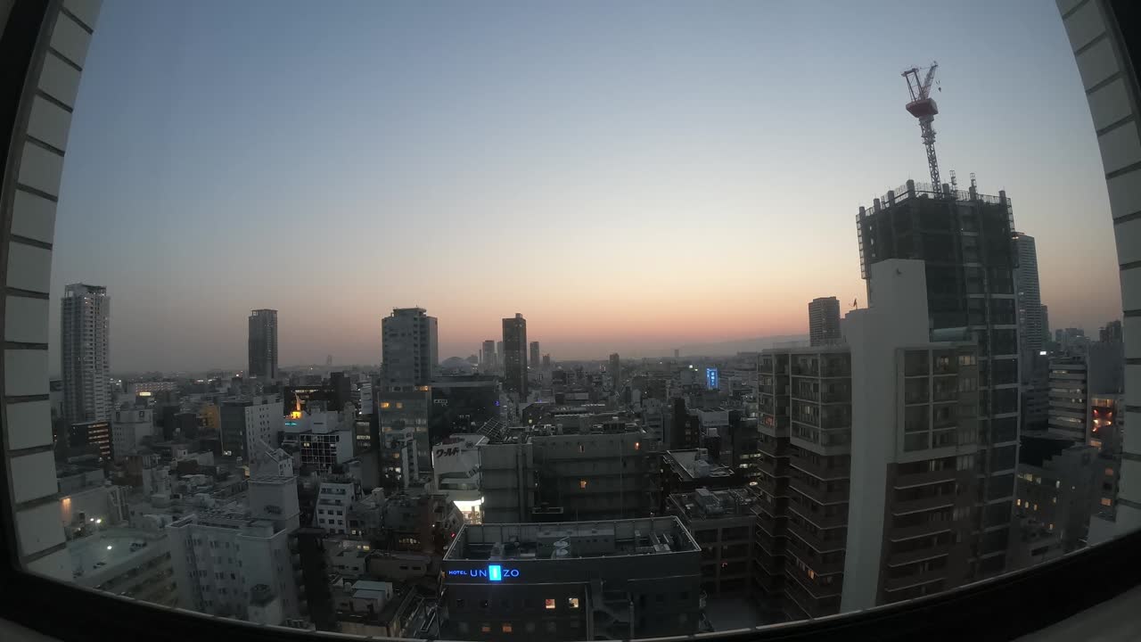 Ultra-wide time lapse of the Osaka skyline buildings going from day to night, Unizo hotel sign visible, locked speed-up shot