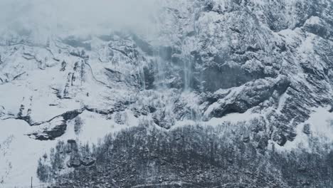 huge avalanche falling down steep rocky mountain in norway, handheld distance view