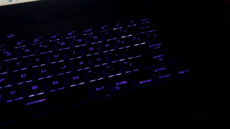 White male hand typing on an RGB laptop keyboard in a dark room and then grabs liquor