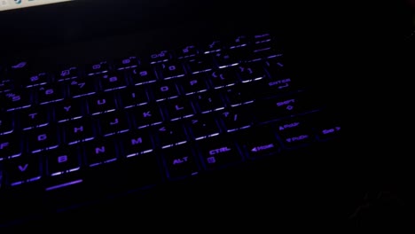 white male hand typing on an rgb laptop keyboard in a dark room and then grabs liquor