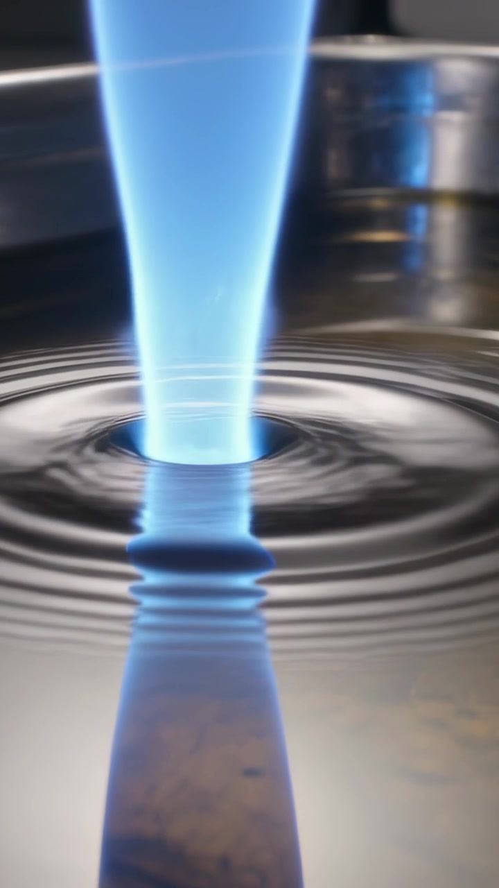 Vertical video: Approaching blue jet hitting liquid in metal pan, creating ripples and reflection