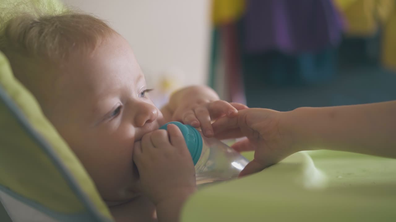 niño con botella de agua en silla alta y hermana mayor en la habitación