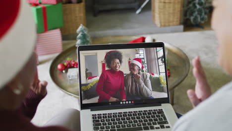 amigas mayores diversas usando una computadora portátil para una videollamada de navidad con amigas sonrientes en la pantalla