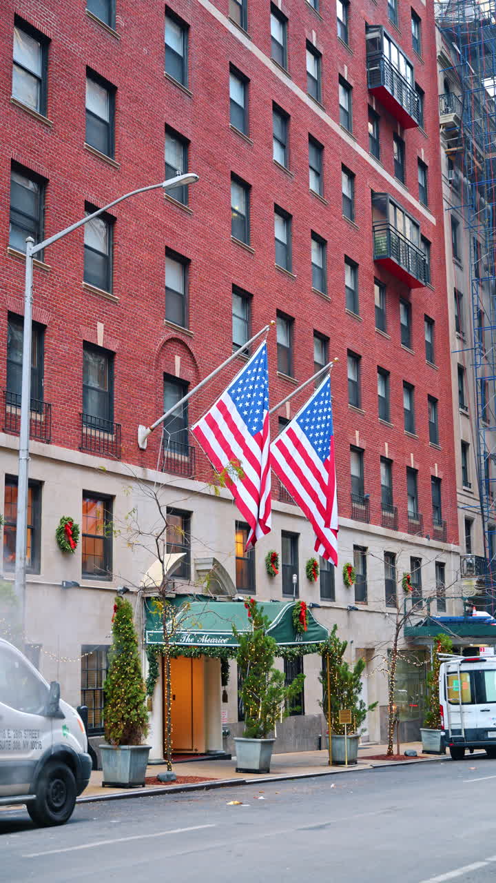 New York, USA, 18 dicembre 2025: Grattacielo in mattoni rossi decorato con bandiere americane all'ingresso. Strada di New York, USA. Video verticale