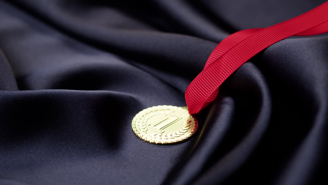 Shiny Gold Medal with Red Ribbon on Dark Fabric