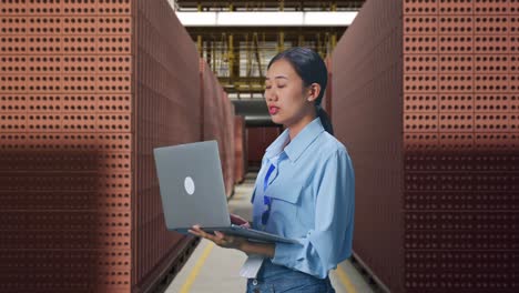 side view of asian female professional worker with red brick packed in stacks are stored, observes by looking up before she come to concentrating on the laptop and keep on typing