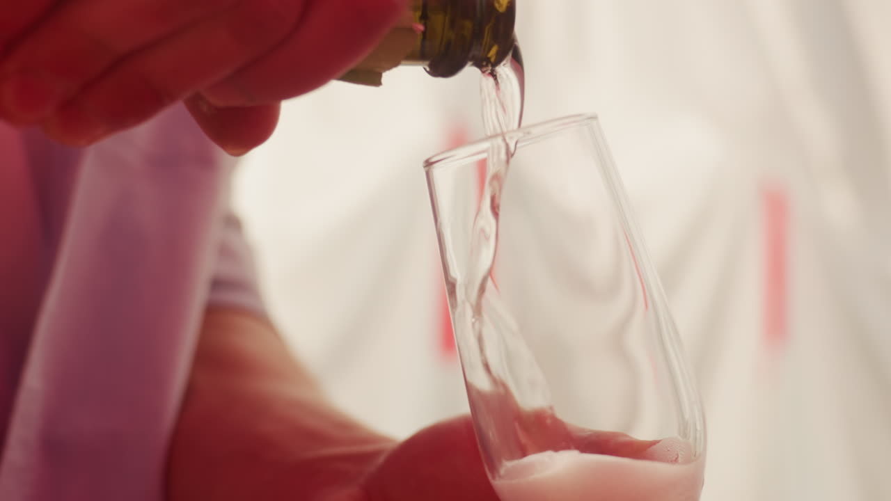 Due flûte di champagne riempite a mano con spumante, versata delicatamente per creare schiuma spumosa e bollicine che salgono, illuminazione calda e soffusa e fondale a tenda, primo piano sul bicchiere e sulla mano, elegante e romantico