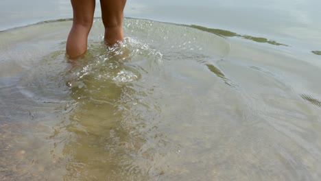 Human-walking-into-clear-water-to-go-swimming-on-a-rocky-beach-in-Croatia,-Europe