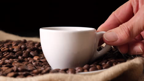 mano de mujer colocando una taza de café en granos de café y yute