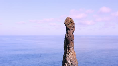 Aerial-orbit-shot-showing-peak-of-rocky-mountain-tower-with-blue-ocean-in-background-during-sunny-day